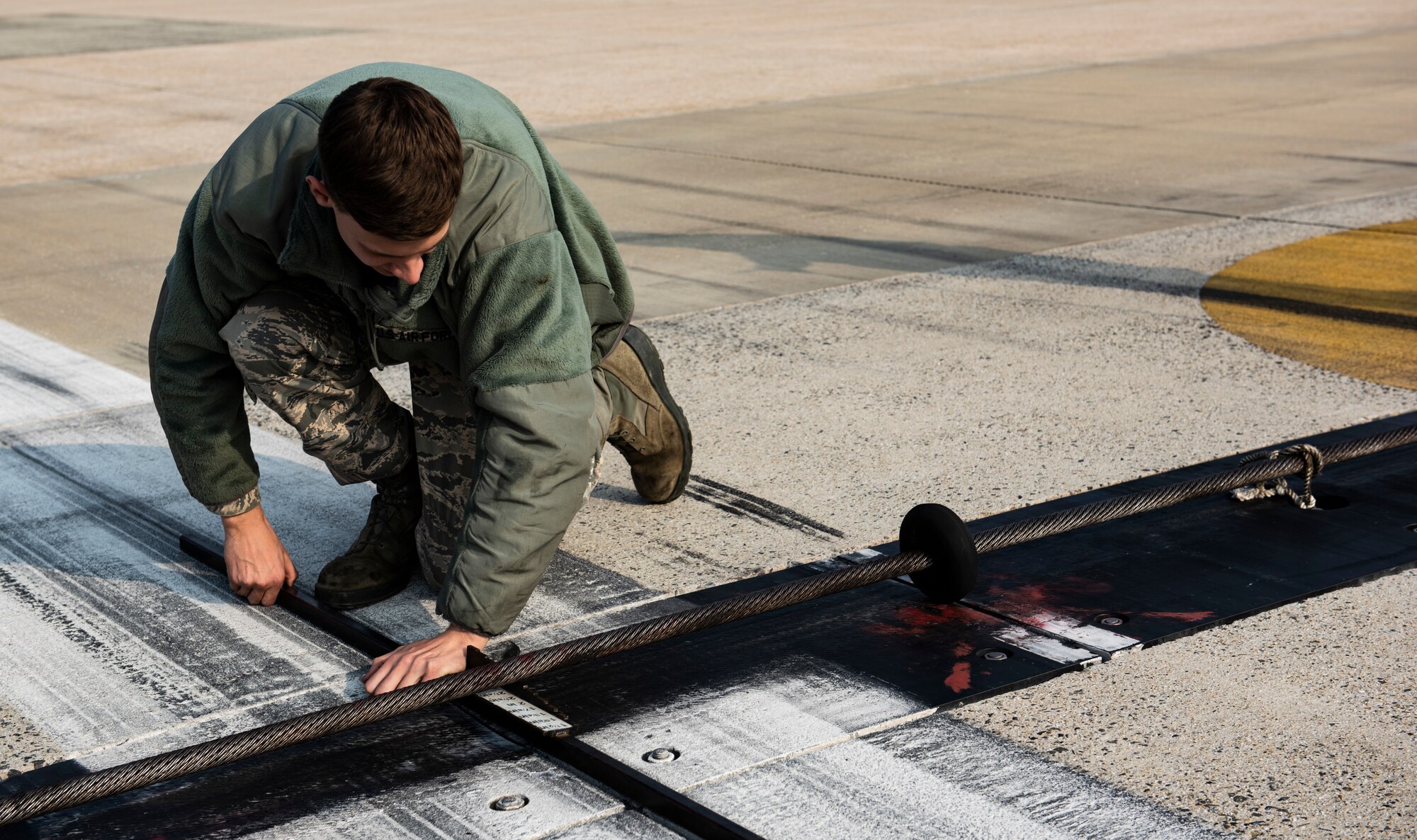 U.S. Air Force Airman 1st Class Zane Mammon, 8th Civil Engineer Squadron electical power production specalis, measures the height of a barrier arresting system at Kunsan Air Base, Republic of Korea, Dec. 19, 2018. The arresting system need to be two inches off the ground to allow enough froom for aircraft to pass over them while still being able to engage it if necessary. (U.S. Air Force photo by Senior Airman Stefan Alvarez)