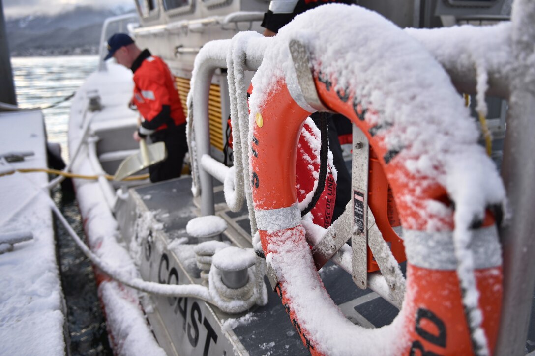 A member of the Coast Guard cleans snow off a boat.