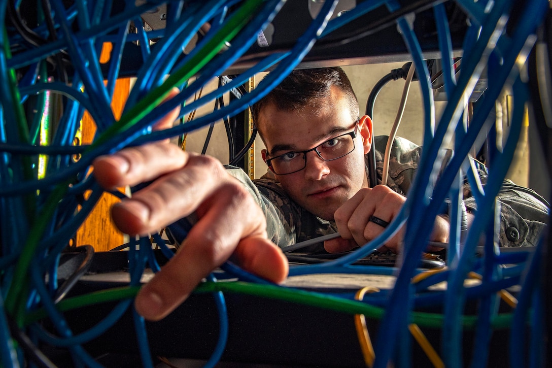 An airman reaches through some cables.