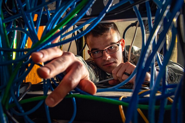 An airman reaches through some cables.