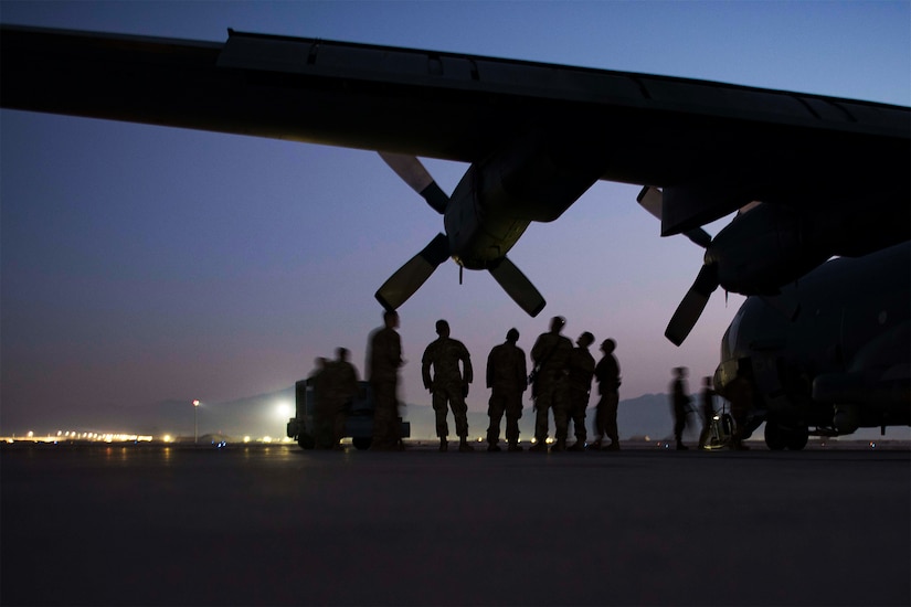 Airmen learn about an aircraft while standing under one of its wings.