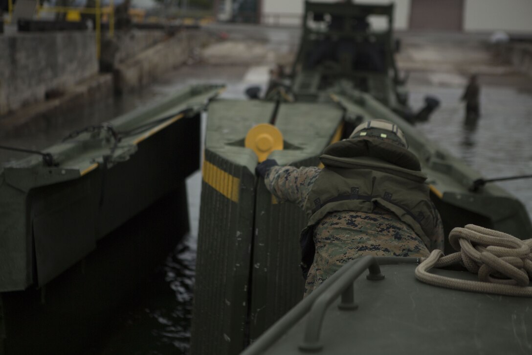 Lance Cpl. Andrew Hollom, a combat engineer with Bridge Company, 9th Engineer Support Battalion, Combat Logistics Regiment 35, reaches for an Improved Ribbon Bridge (IRB) bay to secure it to a Bridge Erection Boat at Naha Military Port, Okinawa, Japan Jan. 31, 2018. Bridge Co. conducted training with IRBs to train new Marines and to show the capabilities of the reactivated company. Hollom is a native of Poplar, Montana. (U.S. Marine Corps photo by Pfc. Jamin M. Powell)