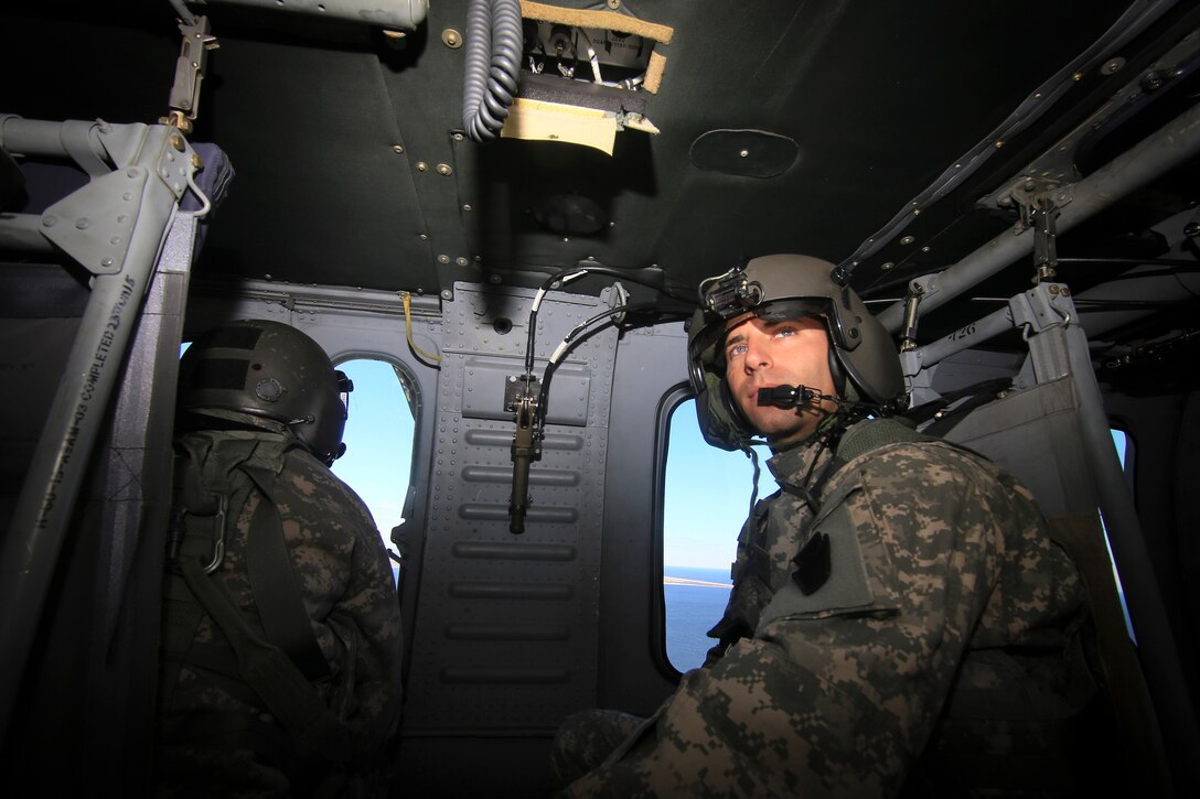 Two guardsmen sit in the back of helicopter.
