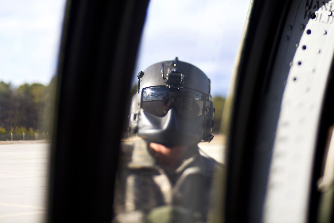 A guardsman wearing a helmet is shown through a helicopter window.