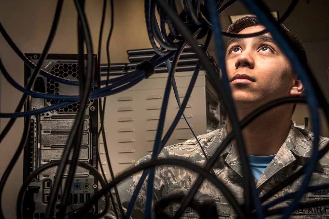 An Airman looks up behind black wires.