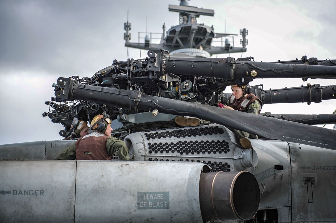 Marines maintain a helicopter engine while on a ship.