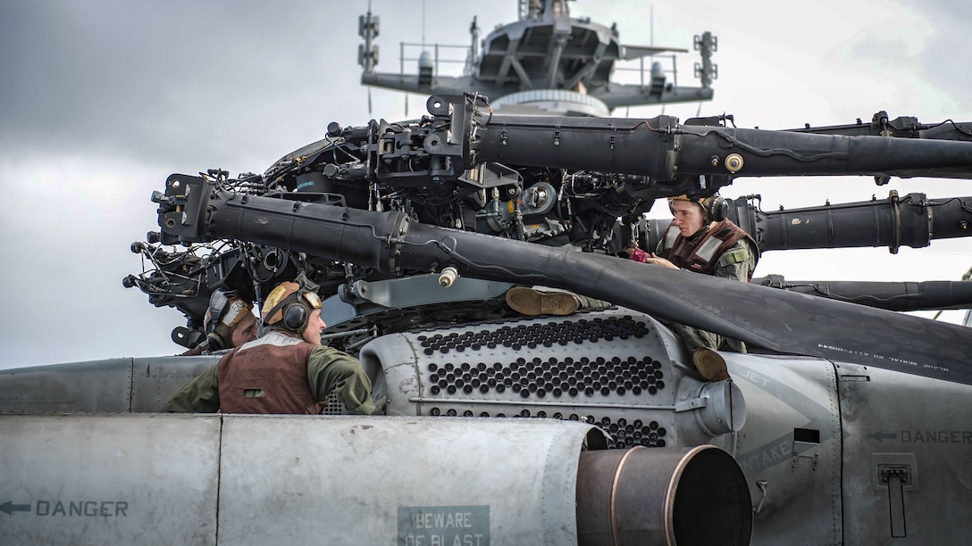 Marines maintain a helicopter engine while on a ship.