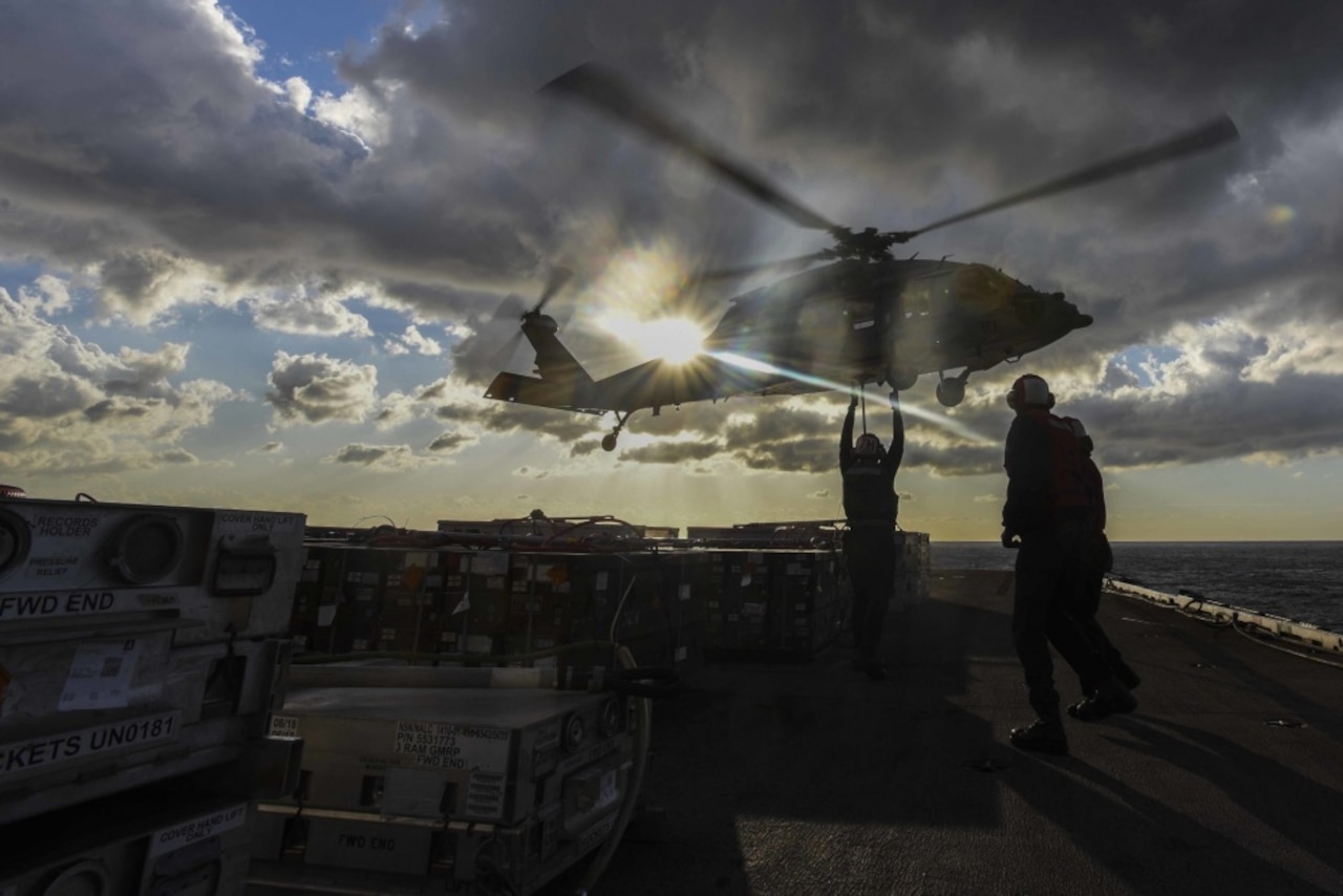 Sailors aboard an aircraft carrier guide a landing helicopter.