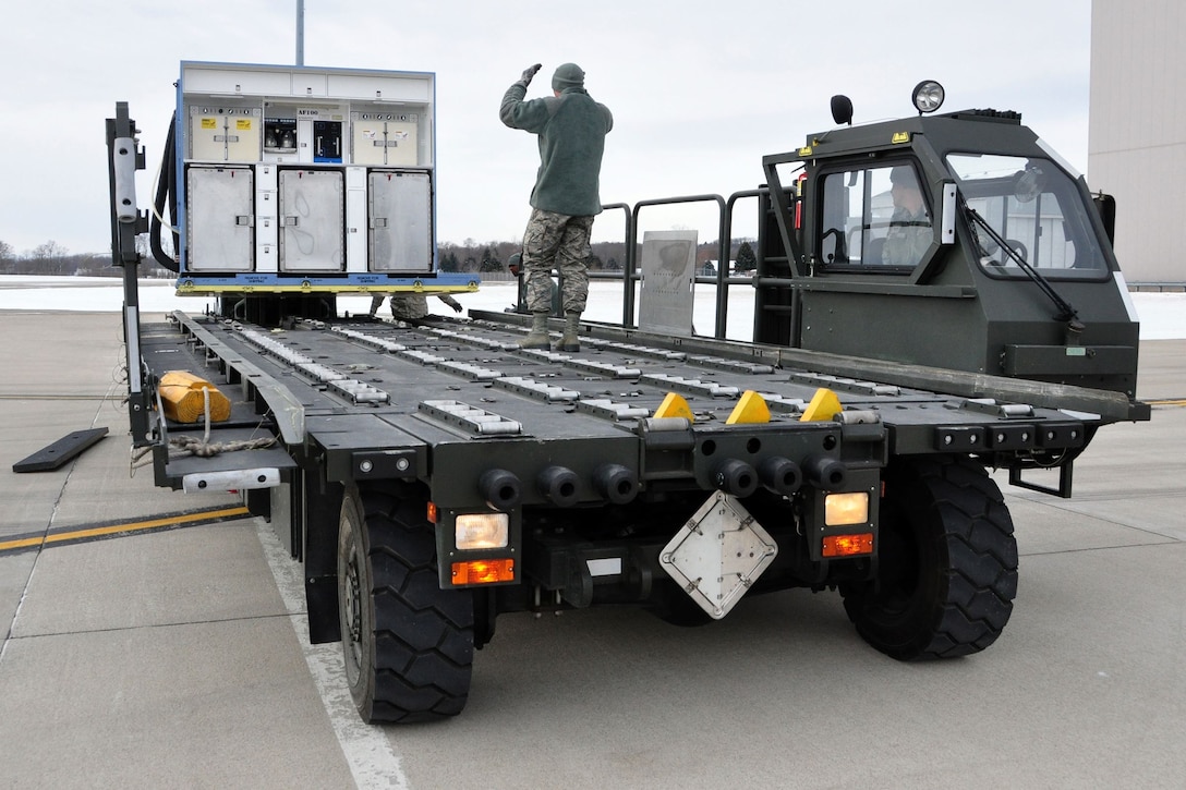 Senior Airman Ryan Hood, 25K Halvorsen Loader driver, looks on as Senior Airman Jacob Dietz, ramp operations journeyman, stands atop the K-Loader to direct the loading of an air transportable galley-lavatory in transit to a C-17 Globemaster III.