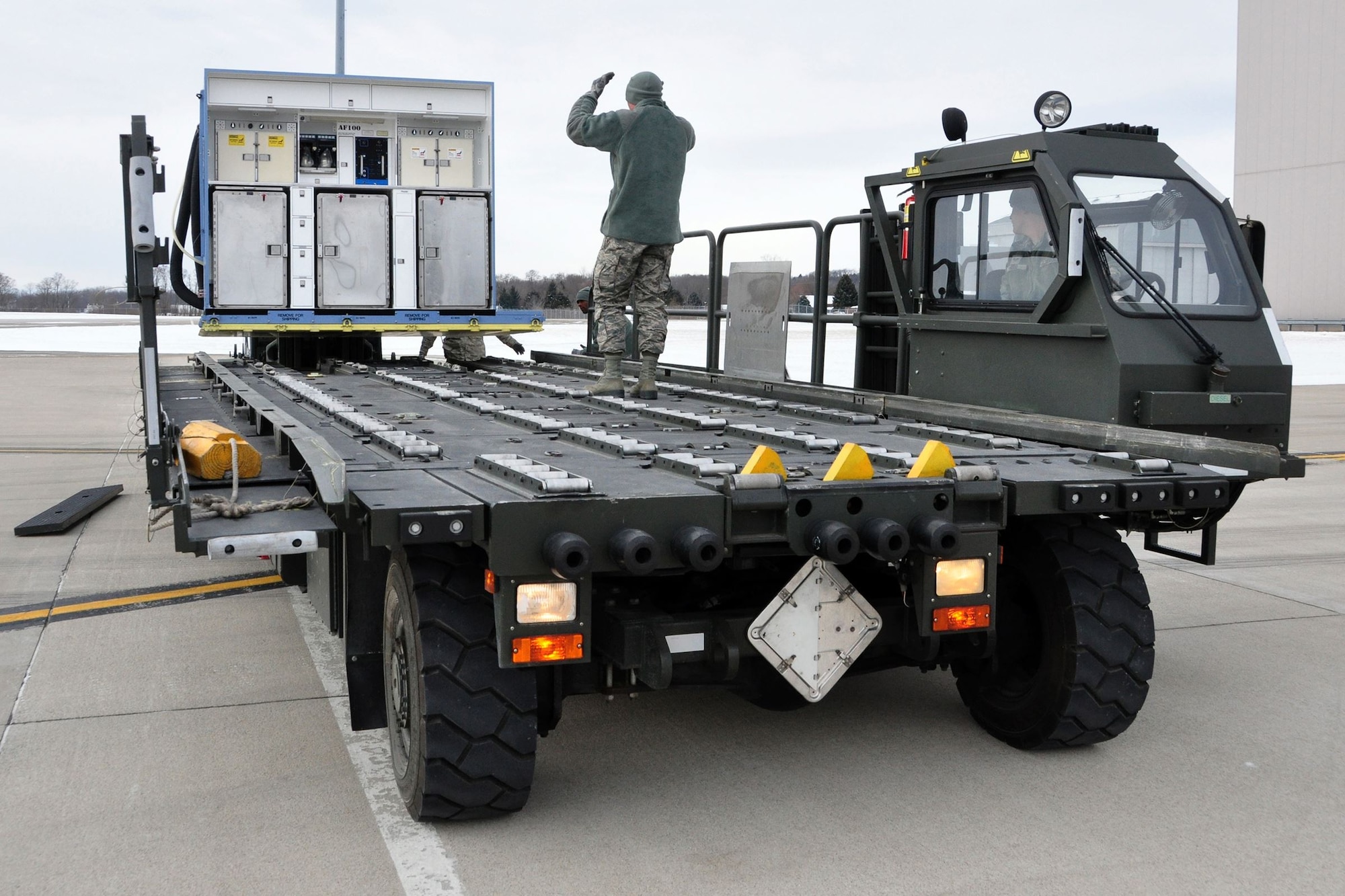 Senior Airman Ryan Hood, 25K Halvorsen Loader driver, looks on as Senior Airman Jacob Dietz, ramp operations journeyman, stands atop the K-Loader to direct the loading of an air transportable galley-lavatory in transit to a C-17 Globemaster III.