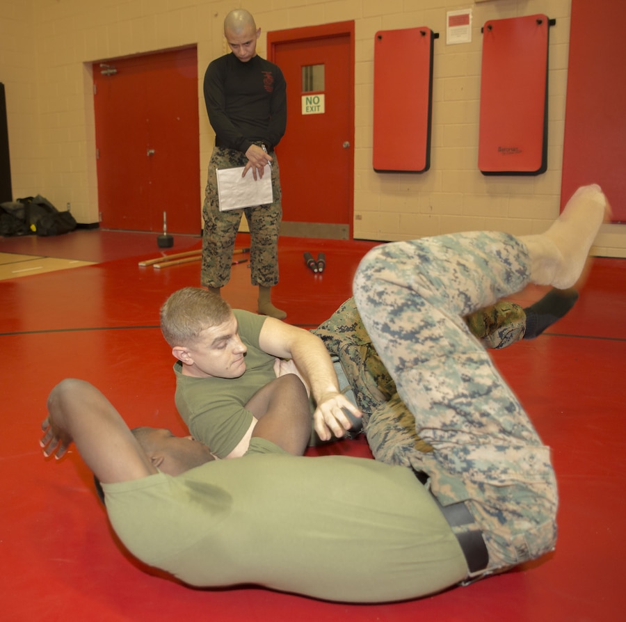 Cpl. Cody Marx, legal services non-commissioned officer, U.S. Marine Corps Forces Command, demonstrates the "arm-bar from guard" technique on Sgt. Lloyd Williams, assistant landing force operational reserve material warehouse chief, G4, MARFORCOM, while Staff Sgt. Frankie Ruiz, warehouse chief, G4, MARFORCOM observes during a Marine Corps Martial Arts Program belt exam at Hopkins Hall gym aboard Camp Allen, Va., Jan. 31. Marx was being tested on several strikes, arm and wrist manipulations, and throws in order to earn his  green belt in MCMAP. (Official U.S. Marine Corps photo by Chris Jones/Released)