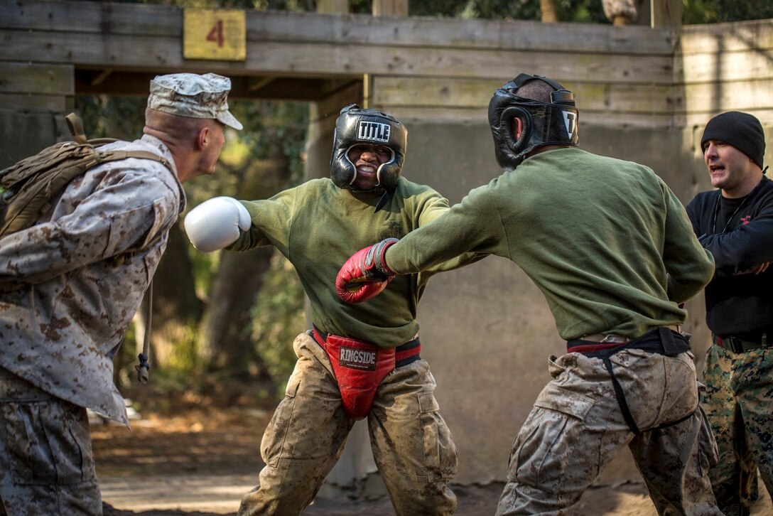 Two recruits in boxing gear spar as two Marines watch and give instructions.
