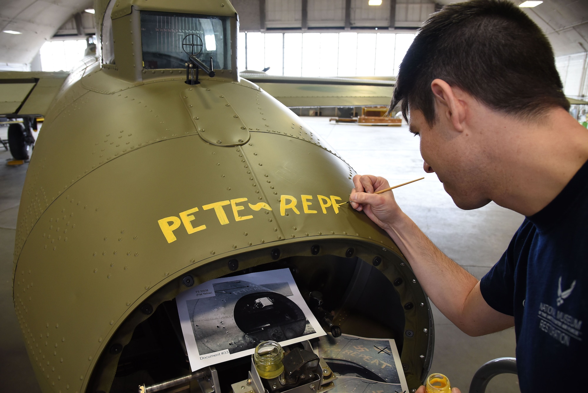 (02/01/2018) Museum restoration specialist Casey Simmons paints the names Pete and Repeat on the tail gun position of the Boeing B-17F Memphis Belle during the restoration process. SSgt. John Quinlan, the tail gunner of the Memphis Belle crew, named the guns Pete and Repeat during WWII. (U.S. Air Force photo by Ken LaRock)