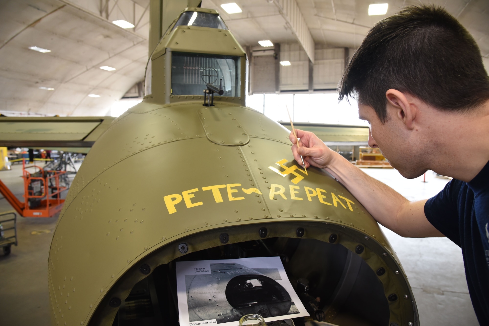 (02/01/2018) Museum restoration specialist Casey Simmons paints the names Pete and Repeat on the tail gun position of the Boeing B-17F Memphis Belle during the restoration process. SSgt. John Quinlan, the tail gunner of the Memphis Belle crew, named the guns Pete and Repeat during WWII. (U.S. Air Force photo by Ken LaRock)