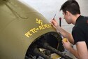 (02/01/2018) Museum restoration specialist Casey Simmons paints the names Pete and Repeat on the tail gun position of the Boeing B-17F Memphis Belle during the restoration process. SSgt. John Quinlan, the tail gunner of the Memphis Belle crew, named the guns Pete and Repeat during WWII. Quinlan also received credit for shooting down one German fighter which is represented by the swastika. (U.S. Air Force photo by Ken LaRock)