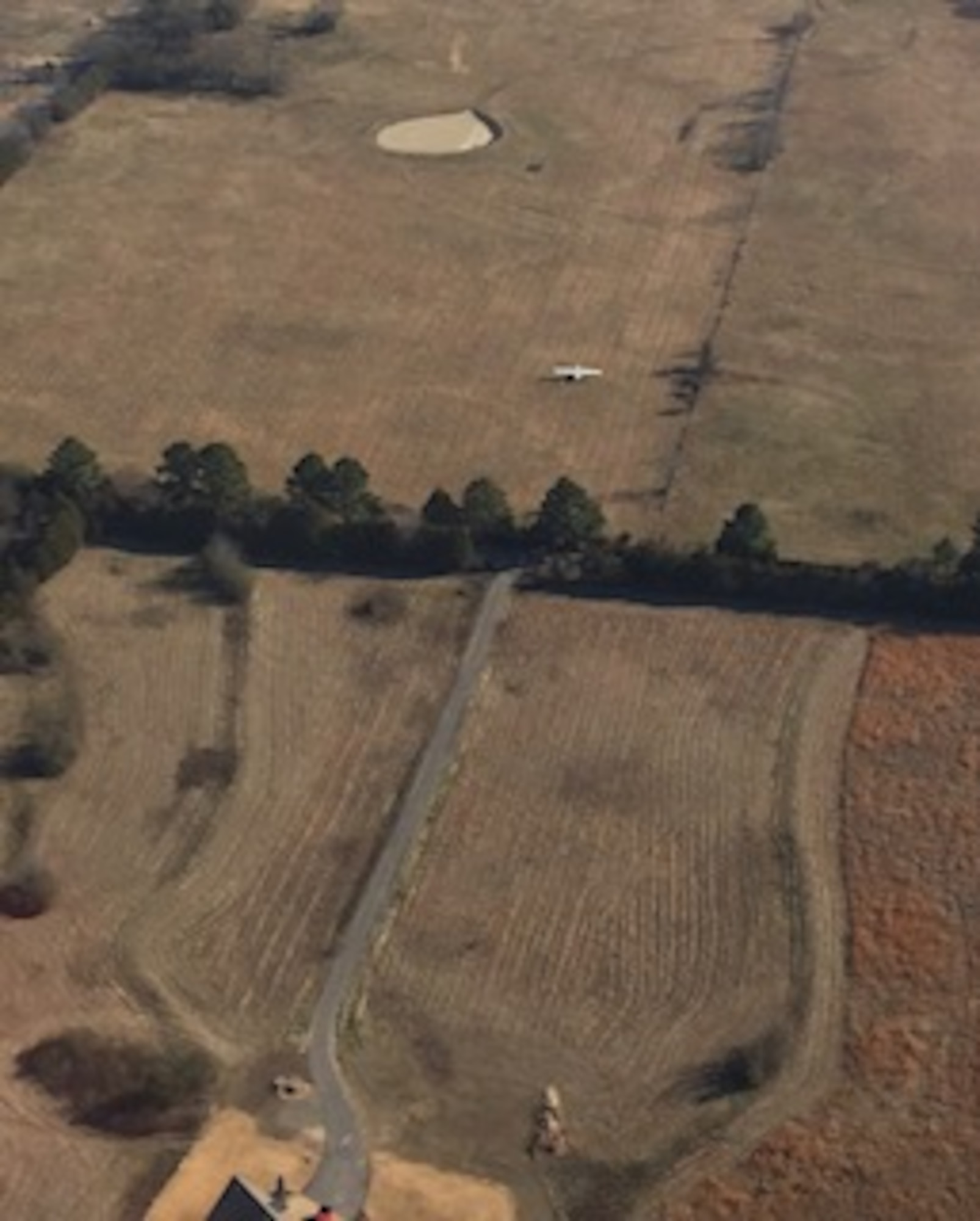 Single engine white Cessna aircraft in the middle of a field as taken from 1500 feet above it.