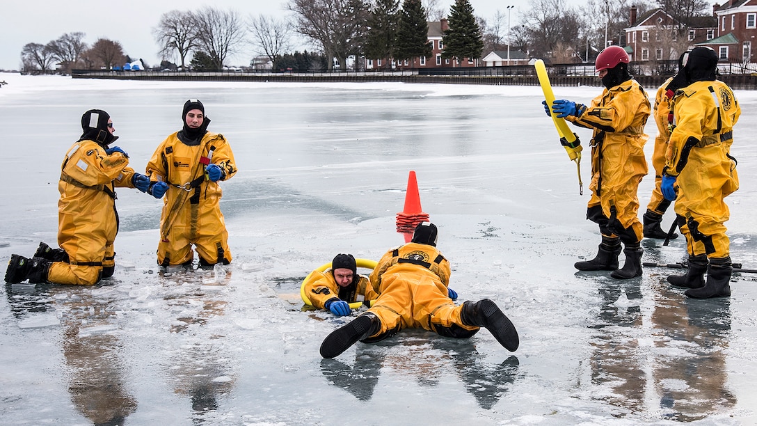 Firefighters in yellow gear practice victim-extraction exercise on ice.