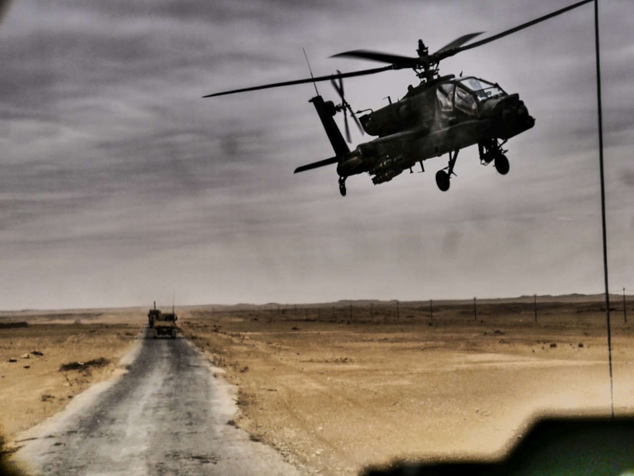 An AH-64 Apache helicopter flies over a convoy in Iraq.