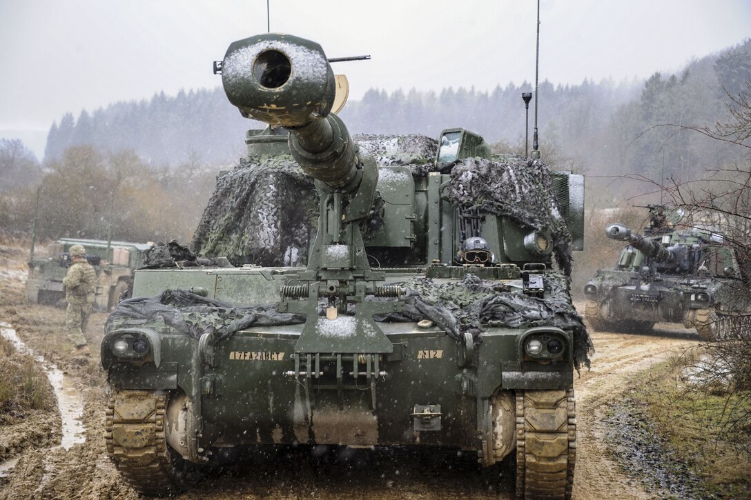 Soldiers maneuver a howitzer on a dirt path.