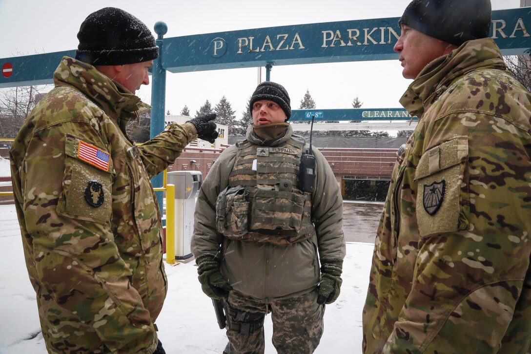 Three soldiers stand and talk outside.