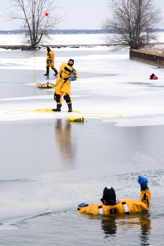 A firefighter throws a rescue rope to a volunteer stuck in a hole in the ice.