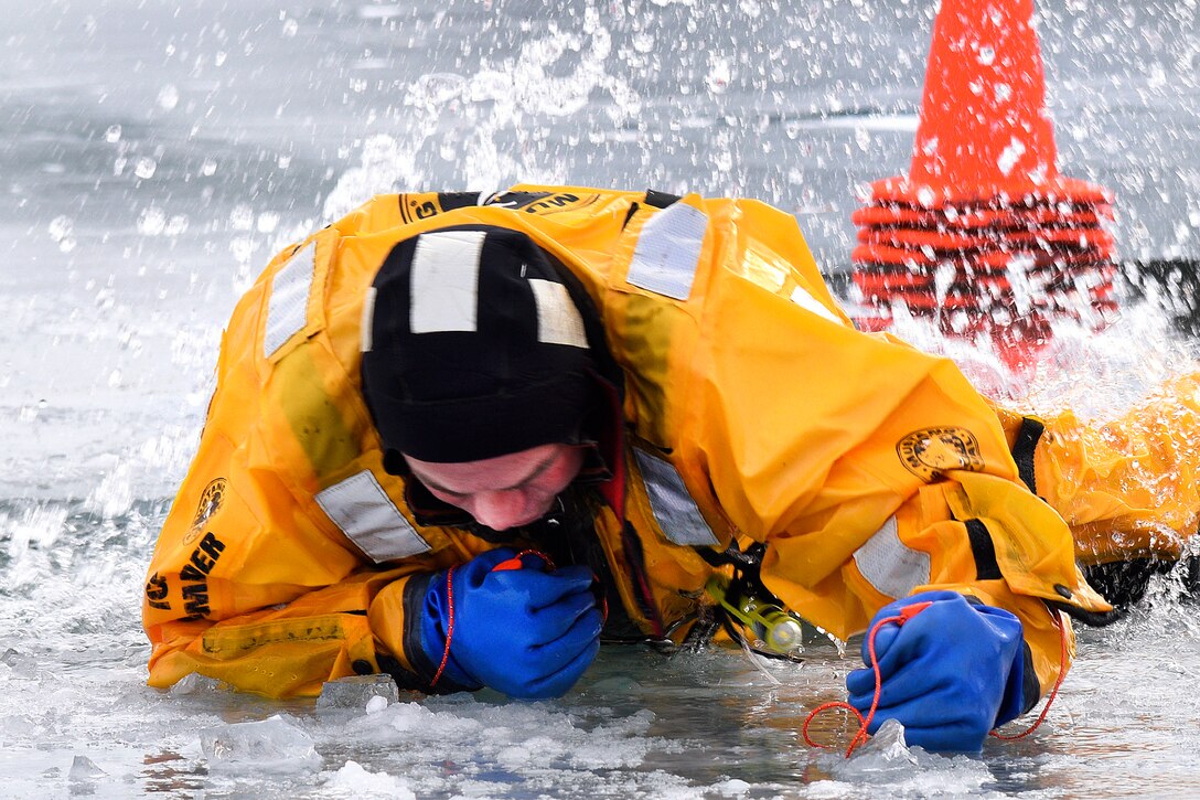 A firefighter pulls himself out of the water onto a frozen lake.