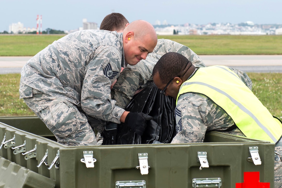 Three airmen unload necessary items from a large crate.