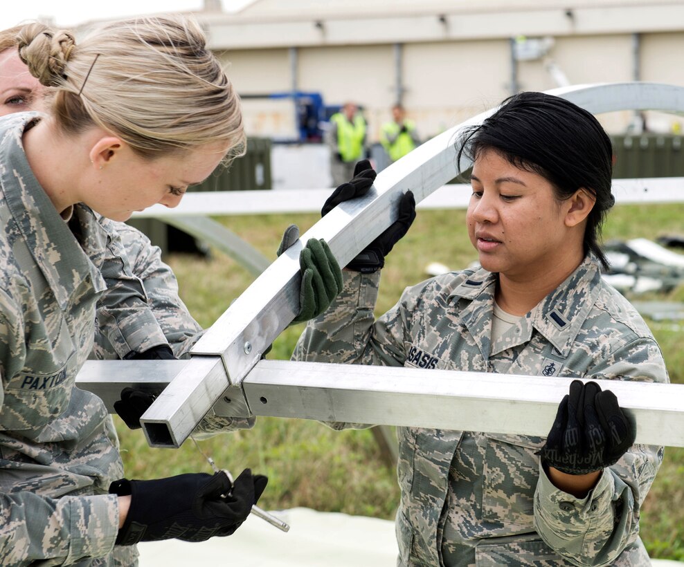 Two airmen assemble the structural framing for a tent near the flightline.