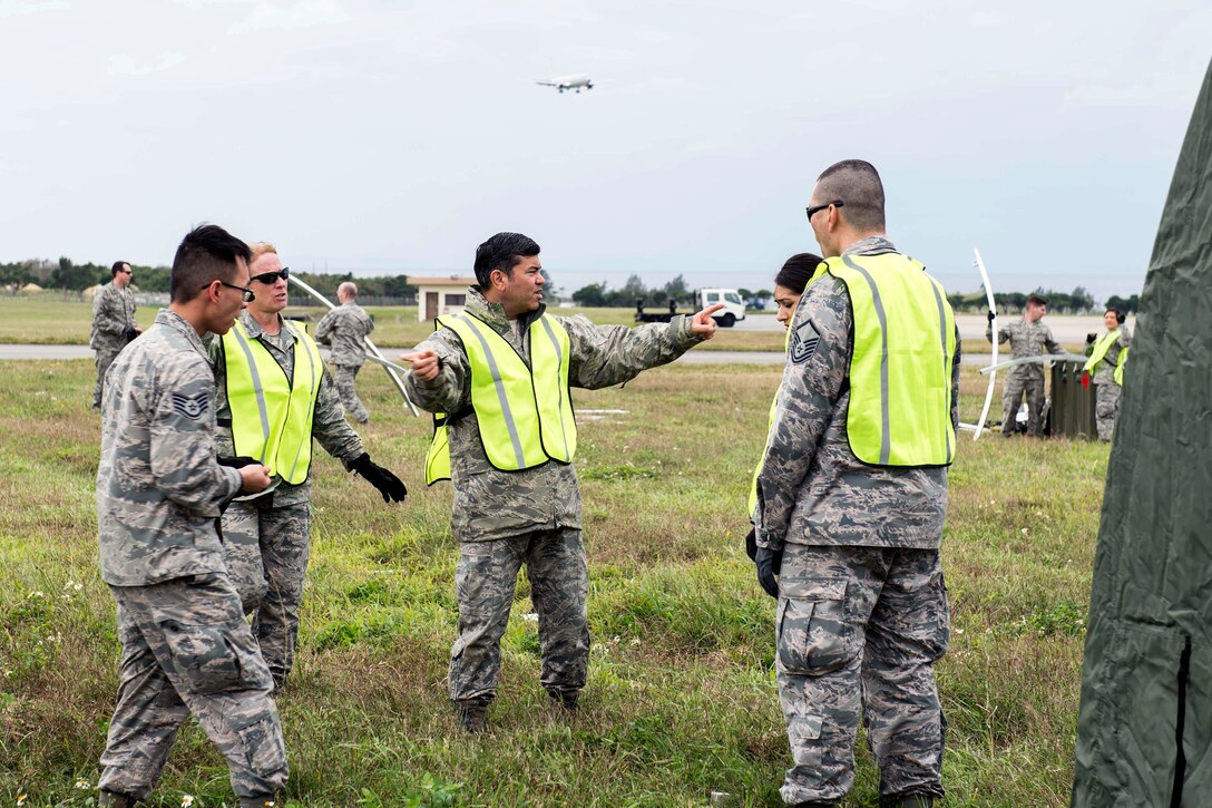 Five airmen stand in a filed near the flightline.
