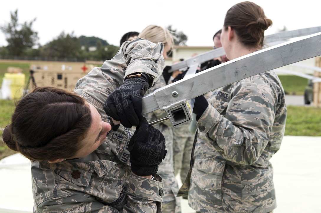 Airmen assemble the structural framing for a tent near the flightline during a field training exercise.