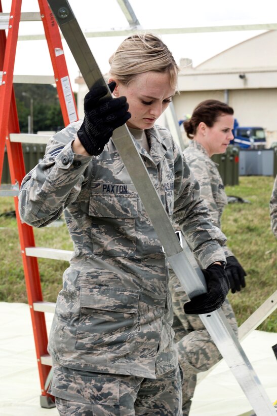 An airman connects parts of structural framing while assembling a tent.