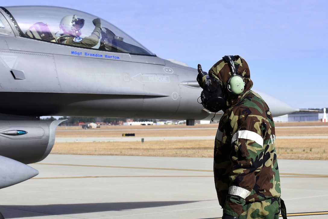 A guardsman wearing a chemical suit gives the thumbs up to a pilot.