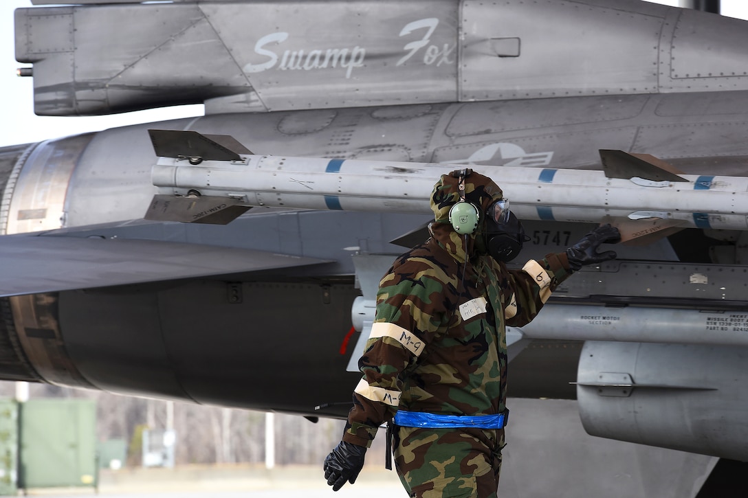 A guardsman wearing a chemical suit checks the munitions on an aircraft.
