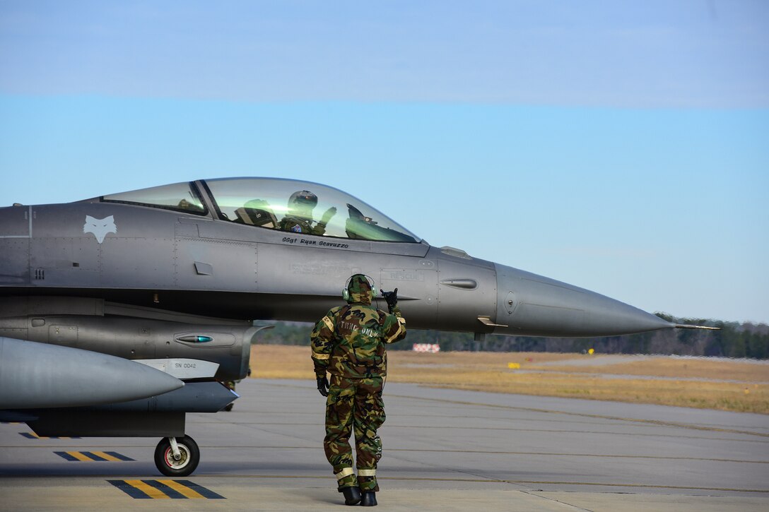 A guardsman wearing a chemical suit gives the takeoff signal to a pilot.