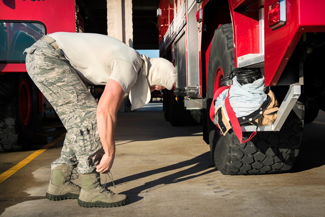 An airman laces his boots while standing next to a firetruck.