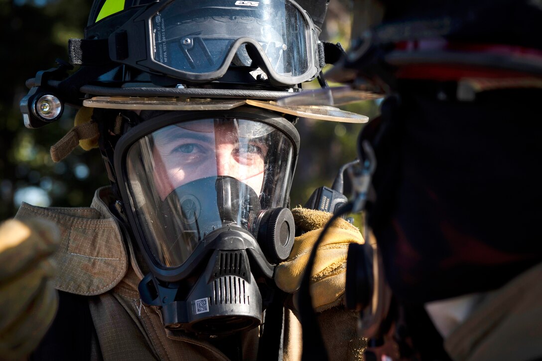 An airman wears a firefighter's helmet and mask.
