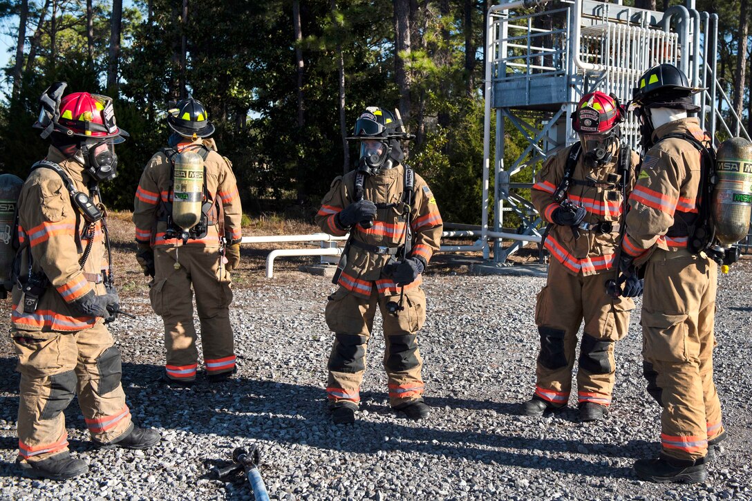 Airmen in full firefighter gear stand in a semicircle.