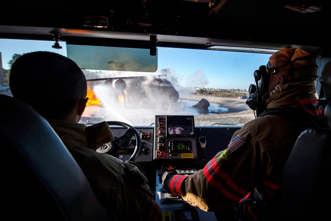 Two airmen sit in a firetruck as they use a hose to put out a fire.