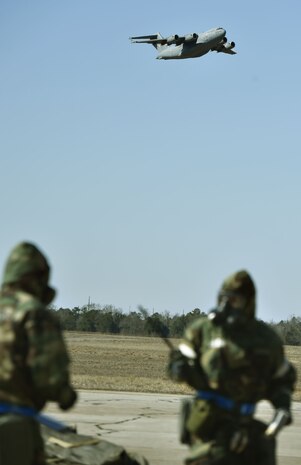 A C-17 assigned to the 437th Airlift Wing flies over Joint Base Charleston’s North Auxiliary Airfield, near Orangeburg, South Carolina, as U.S. Air Force Airmen of the 321st Contingency Response Squadron, 621st Contingency Response Wing, sweep a mock camp for simulated unexploded ordnance during Exercise Crescent Moon Jan. 30.