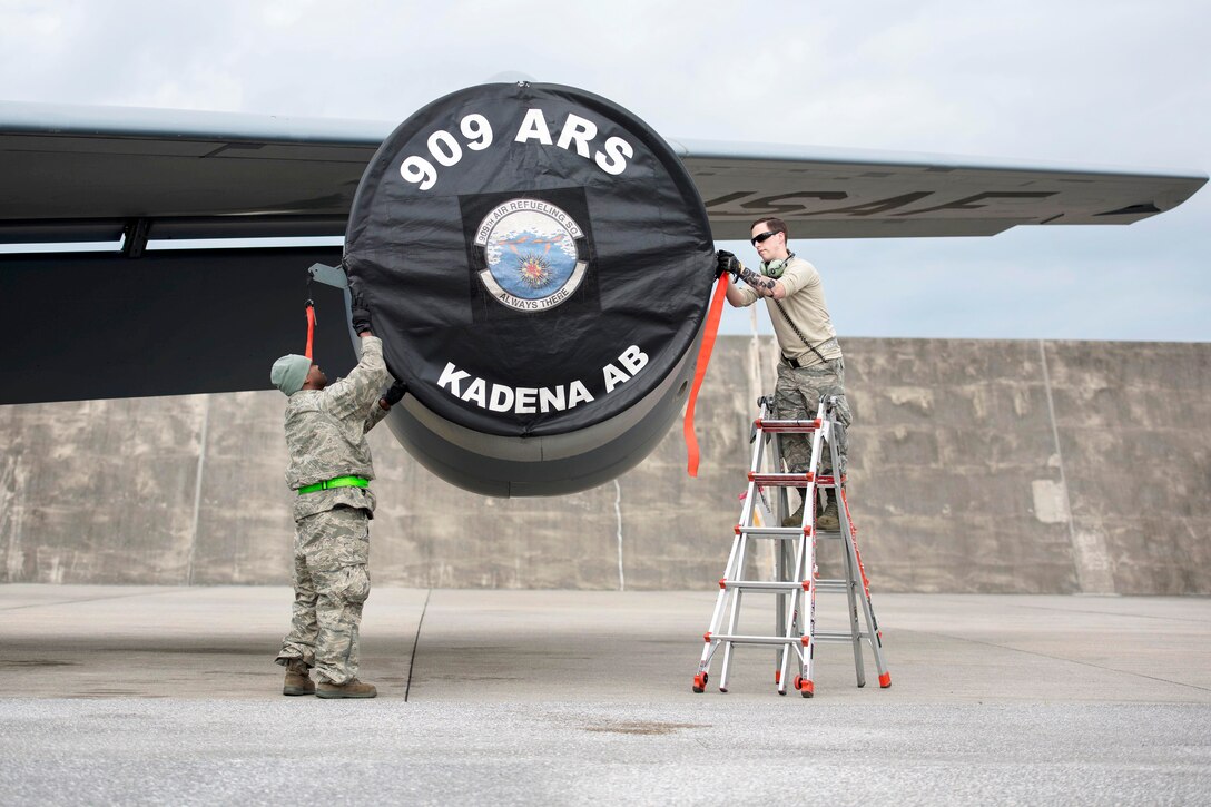 Two airmen place an engine cover on an aircraft.