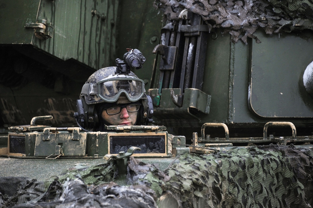 A soldier 's head appears out of a hole in an M109A6 Paladin howitzer.