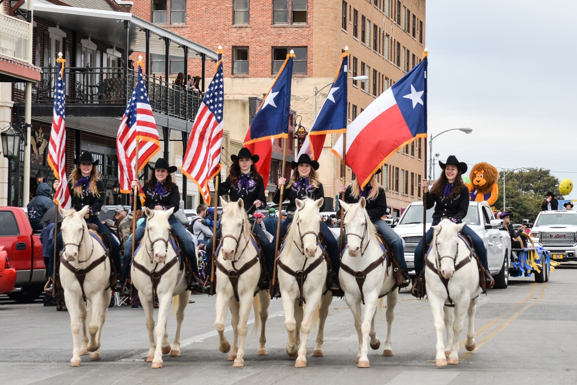 Six white horses and their riders carry American and Texas flags during the rodeo parade in San Angelo, Feb. 3. 2018. The rodeo parade featured 100 entries and included members of the Sante Fe Trail Ride, various floats from clubs and community organizations, antique tractors and local horse clubs. (U.S. Air Force photo by Aryn Lockhart/Released)