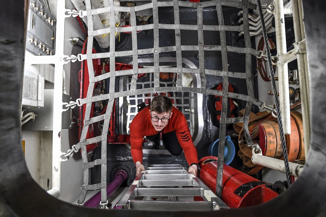 A sailor in red, viewed from above, climbs a ladder up a ship's passageway, framed by criss-crossed netting,