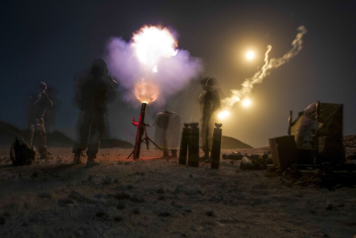 A blast from a mortar lights up the night sky, as soldiers stand by the weapon.