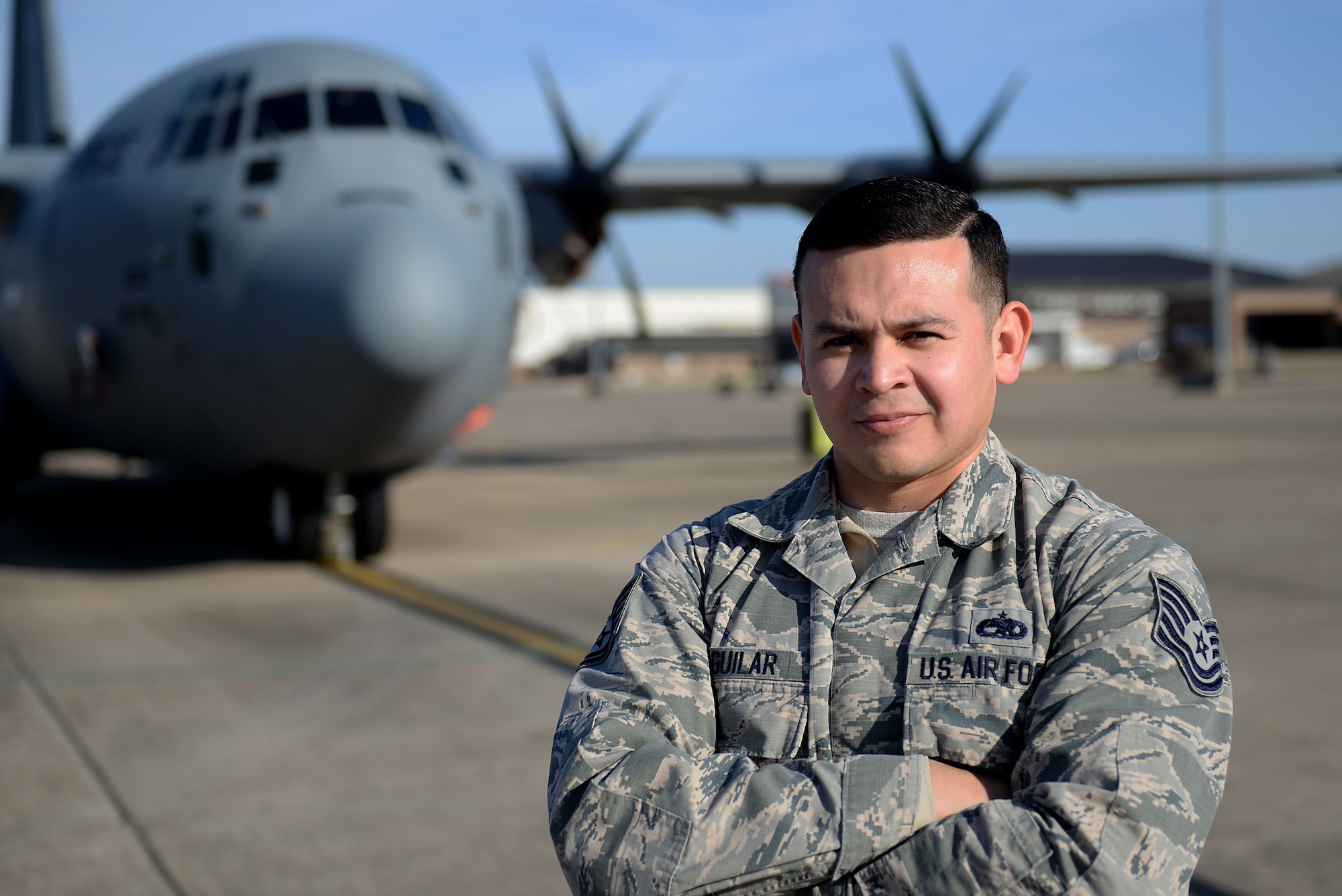 A man in the Air Force Battle Uniform stands with his arms folded in front of a C-130J.