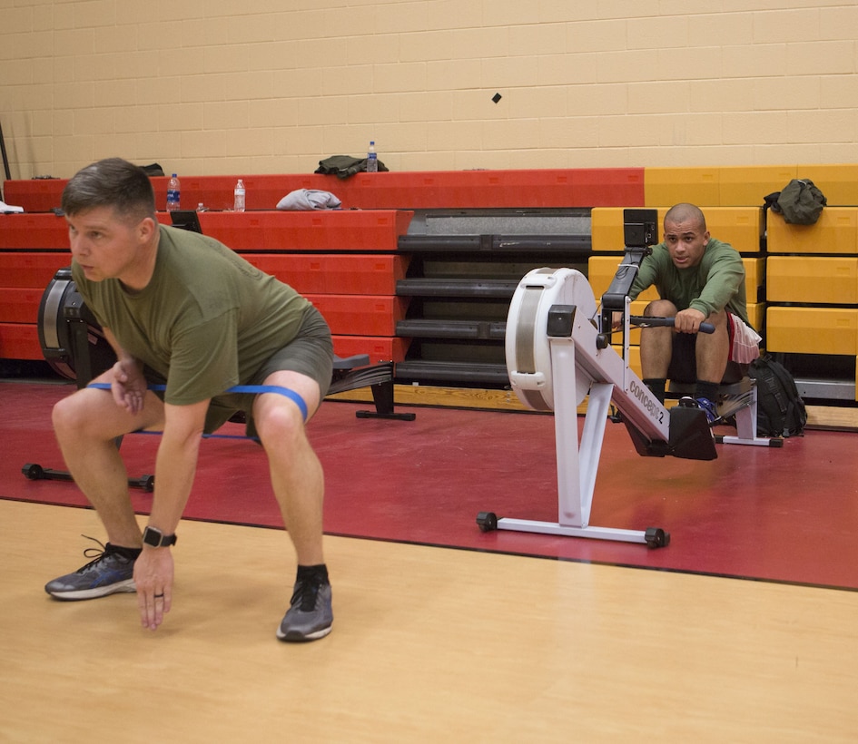 Master Sgt. Jeremy Owens, battalion logistics chief, Headquarters and Service Battalion, U.S. Marine Corps Forces Command, squats with a resistance band while Sgt. James Toney, security specialist, MARFORCOM, uses the rowing machine during a High Intensity Tactical Training session at Hopkins Hall Gym aboard Camp Allen, Va., Feb. 1. Marines worked with a partner, switching between exercises at each station. (Official U.S. Marine Corps photo by Chris Jones/Released)