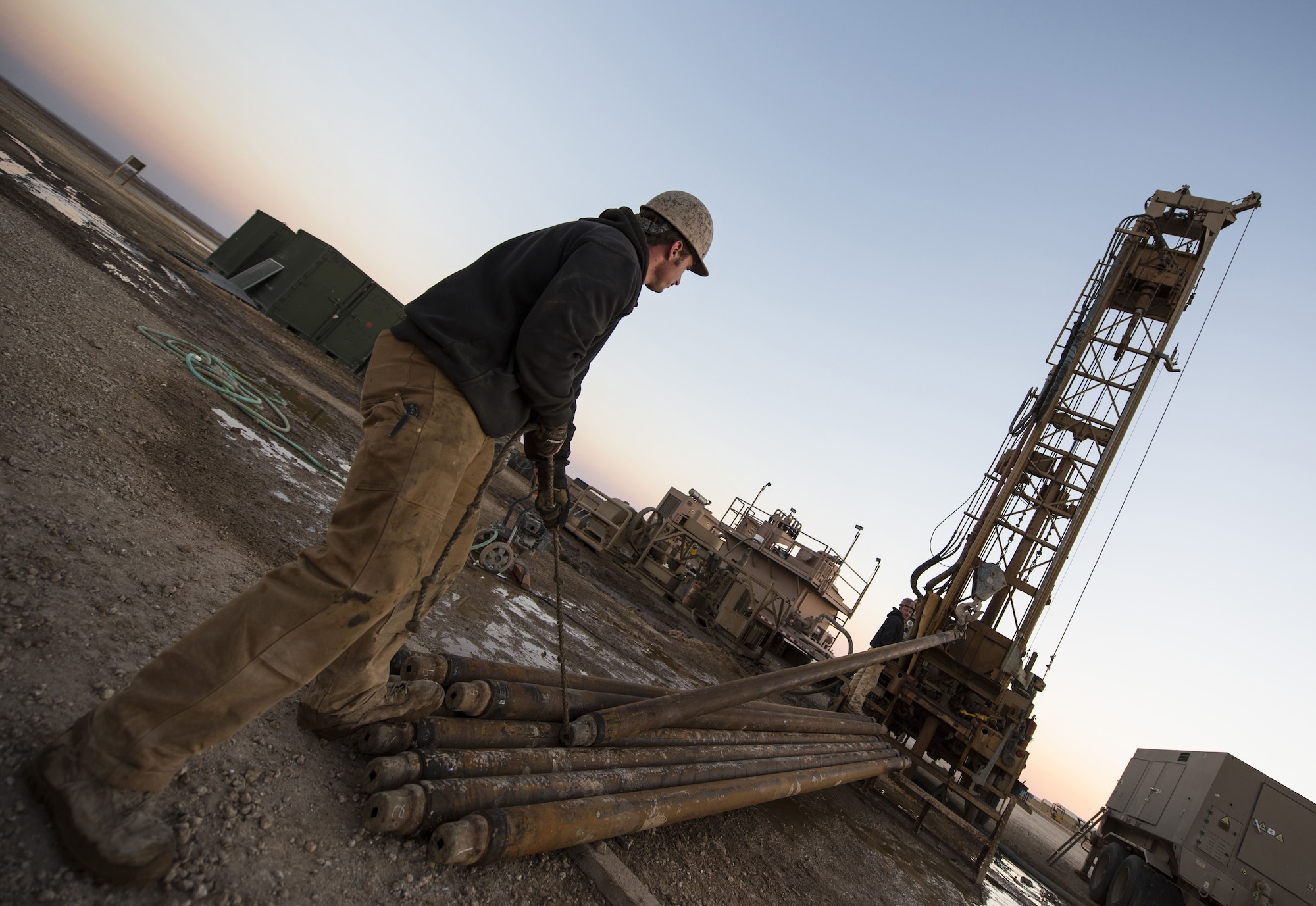 SSgt Zachary Gosteli, a vehicle mechanic assigned to the 557th Expeditionary RED HORSE Squadron, guides heavy steel piping into position on a well drilling site January 31, 2018 at an undisclosed location in Southwest Asia. The crew removed piping in order to gain access to screens, which gradually filter groundwater as it rises to the top. (U.S. Air Force photo by Staff Sgt. Joshua Kleinholz)