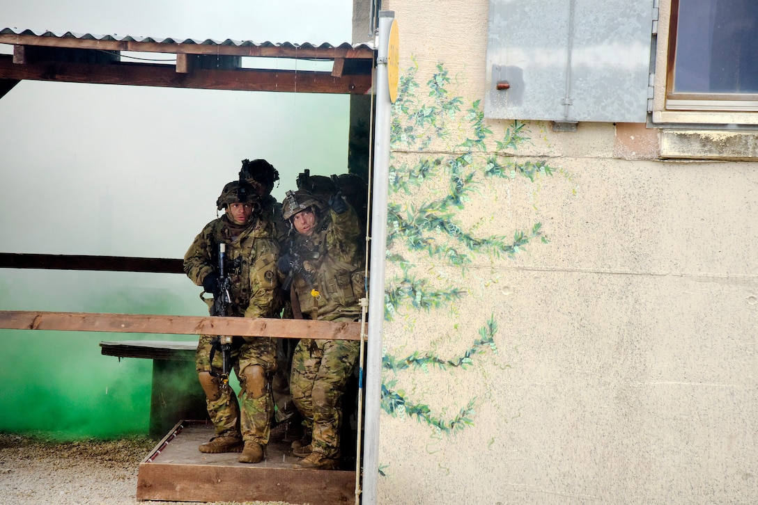 Soldiers stand outside of a building with rifles.