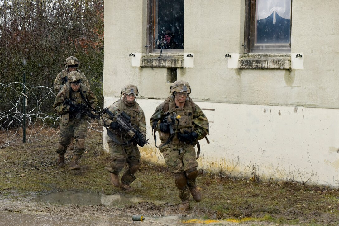 Soldiers carry rifles as they run around the corner of a building.