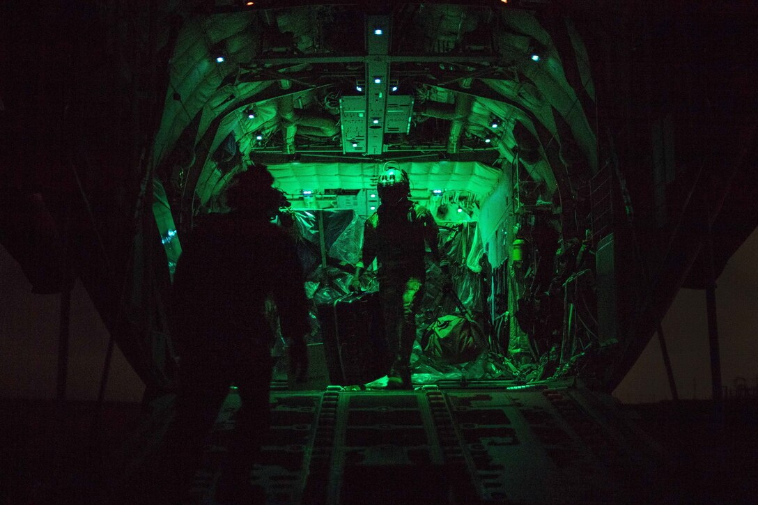 Two airmen load cargo into the back of an aircraft under a green light.
